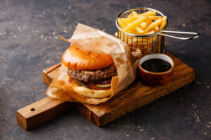 Burger with meat and French fries in serving basket on dark background